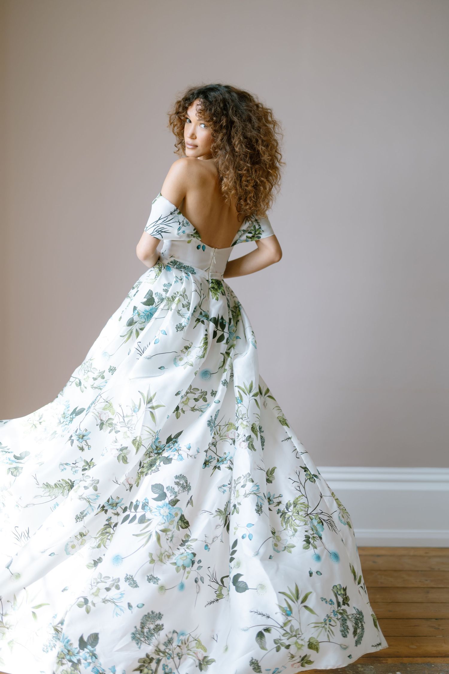 An elegant floral gown with a flowing skirt twirls against a neutral backdrop.