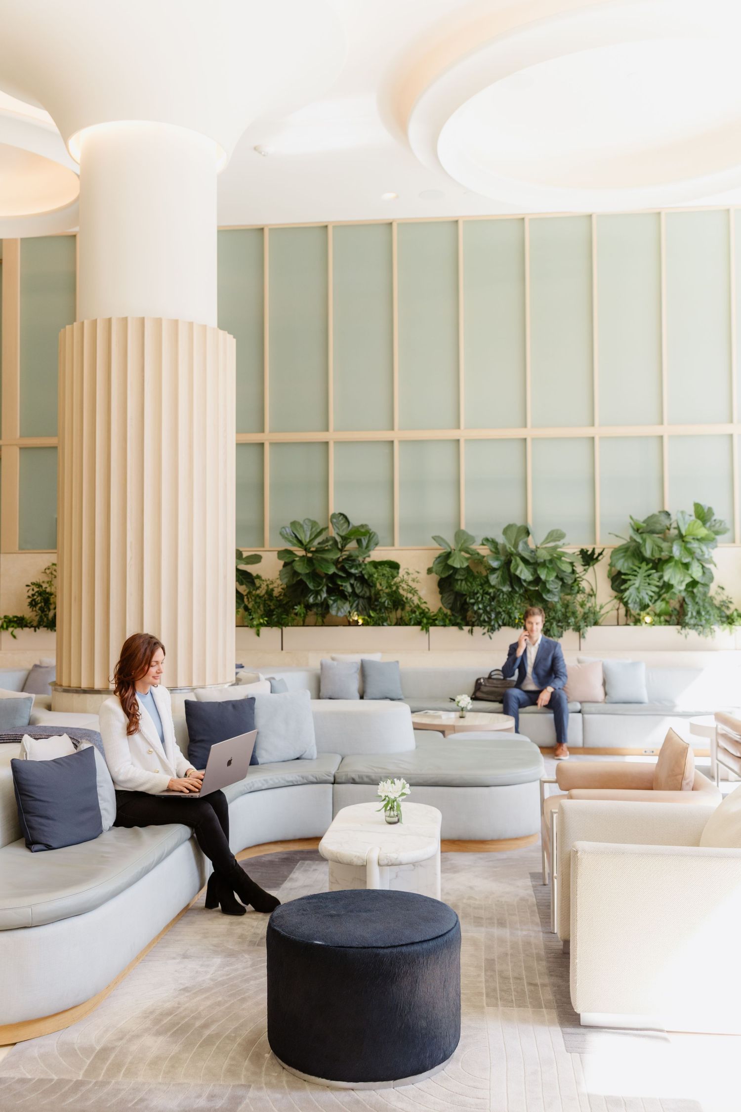 Modern hotel lobby with plush curved seating, fluted columns, and green wall accents creates an elegant lounge atmosphere.
