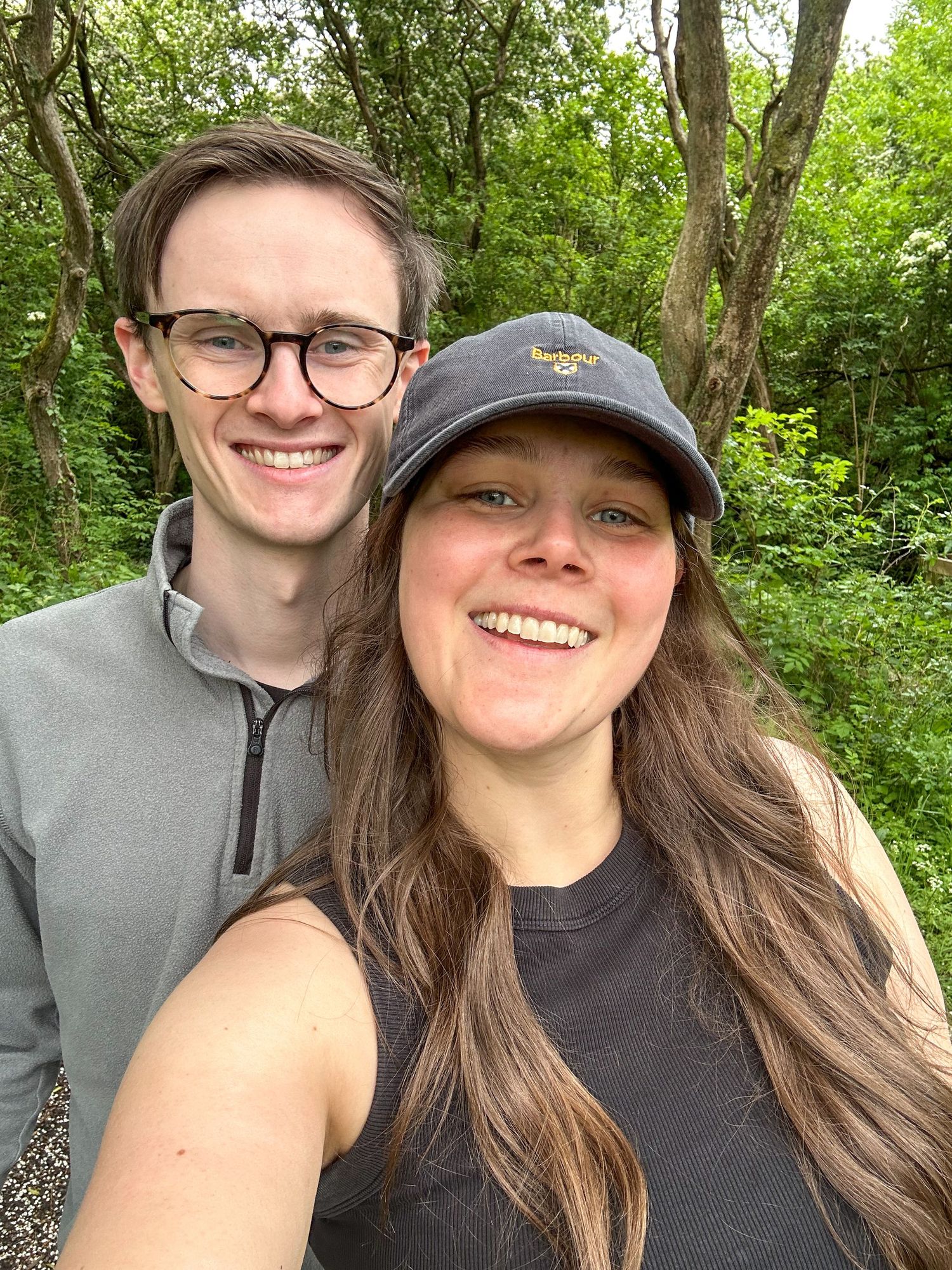Outdoor selfie of a couple among green foliage on a sunny day.