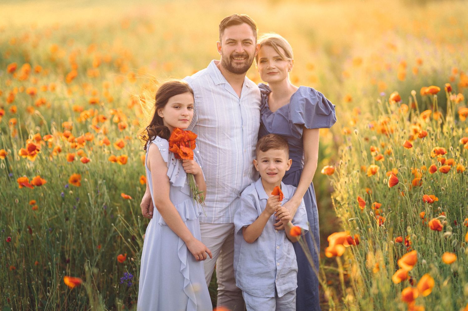 A family stands together in a blooming orange poppy field during golden hour sunset.