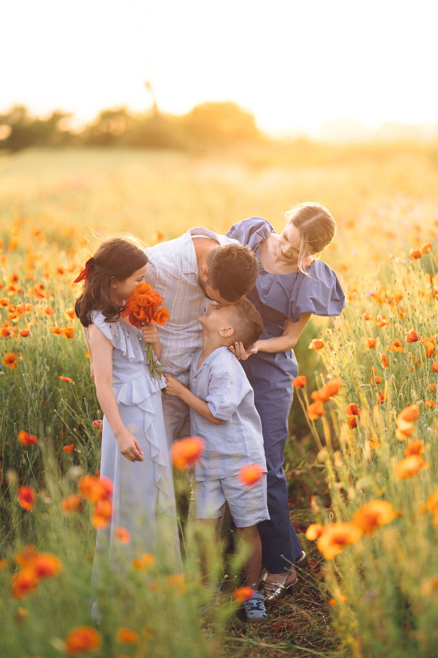 Three young children in light clothing explore a blooming orange poppy field during golden sunset hour.