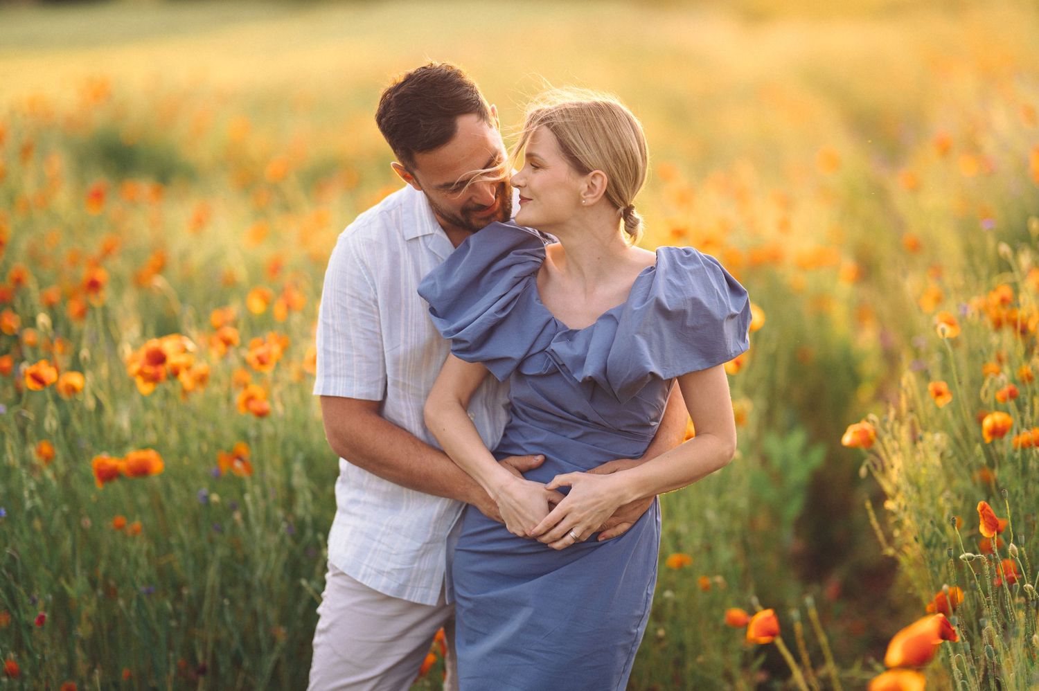 Couple embraces tenderly in a meadow of vibrant orange poppies during golden hour sunset.