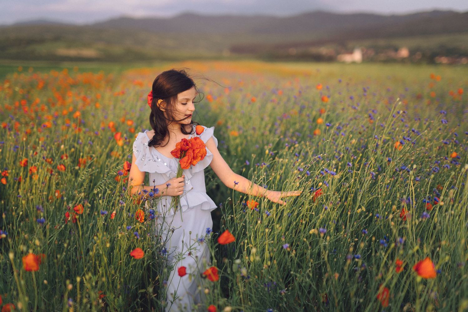 Person dressed in white joyfully runs through a vibrant field of red poppies and green grass against rolling hills.
