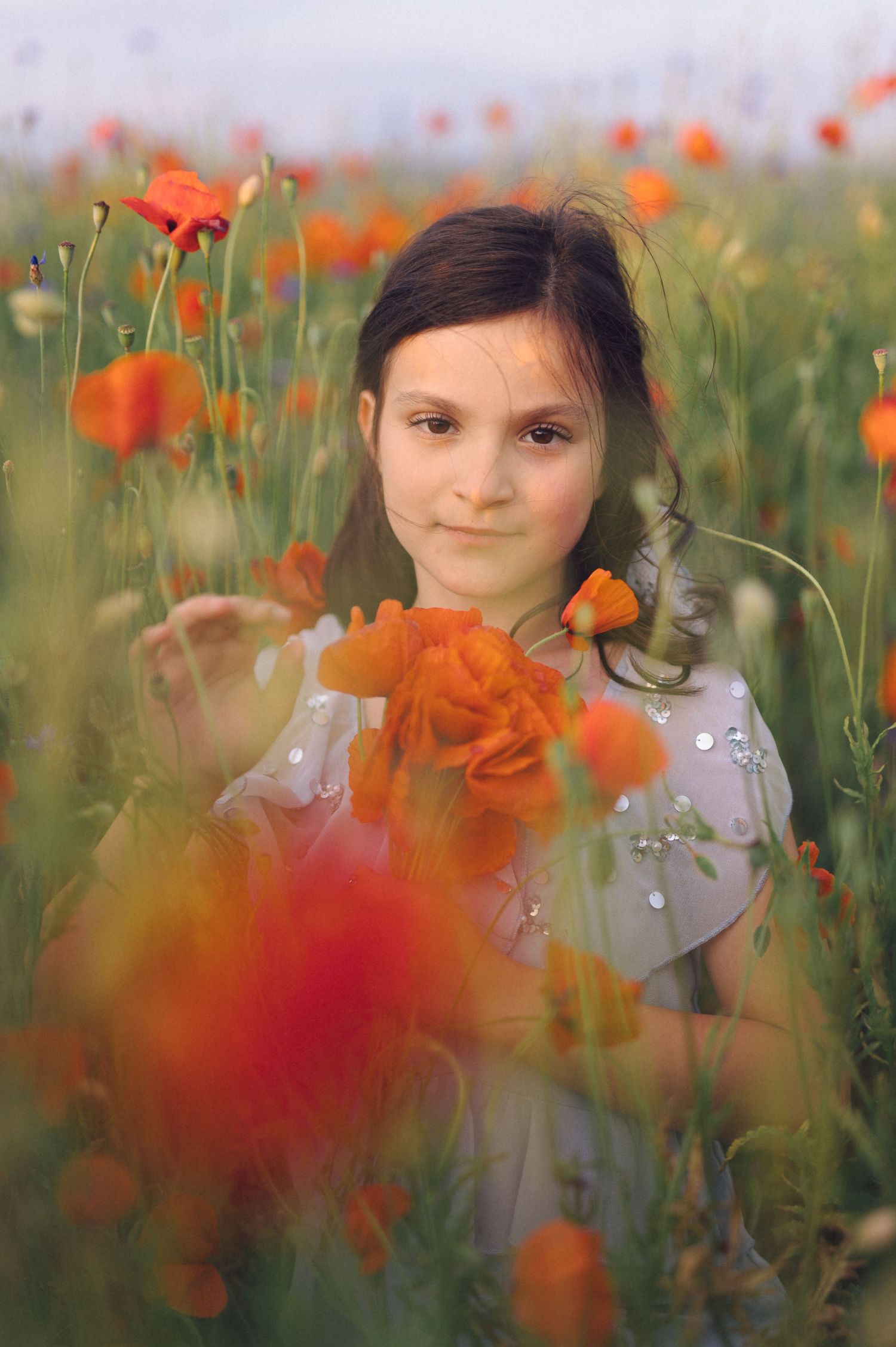 A girl in a floral spring dress stands amidst a vibrant field of blooming orange poppies on a sunny day.
