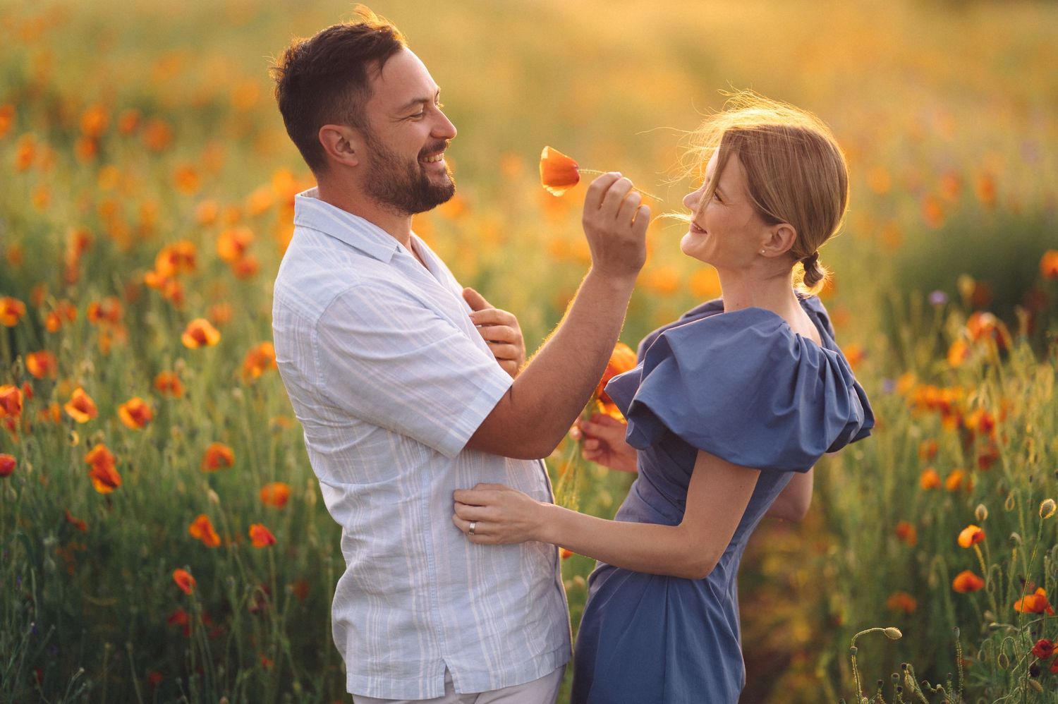 A couple in a golden wildflower field enjoy a tender moment as sunlight bathes them in warm light.