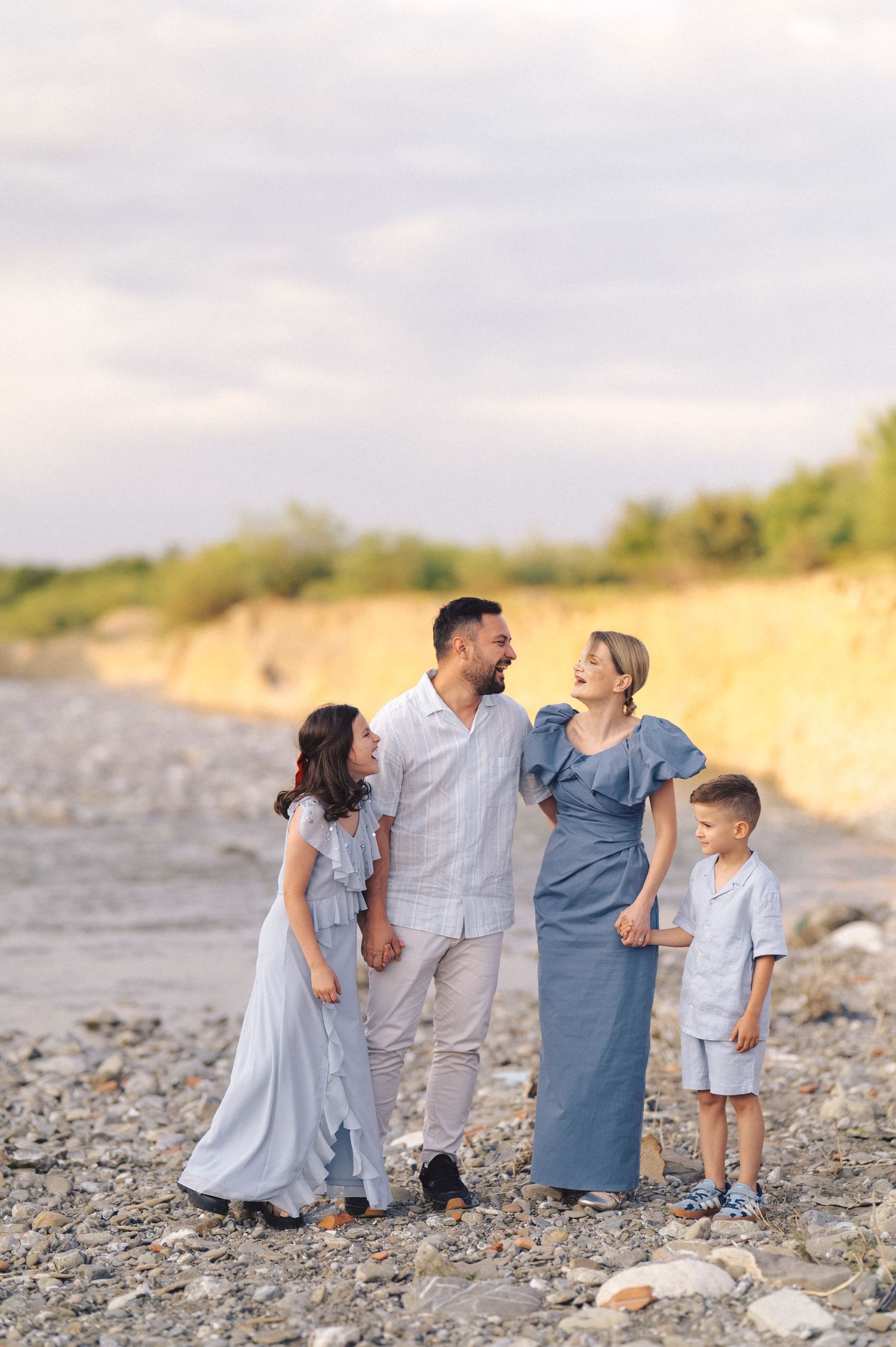 Family in coordinated blue and white outfits walking together on a rocky beach at sunset with cliffs in background.