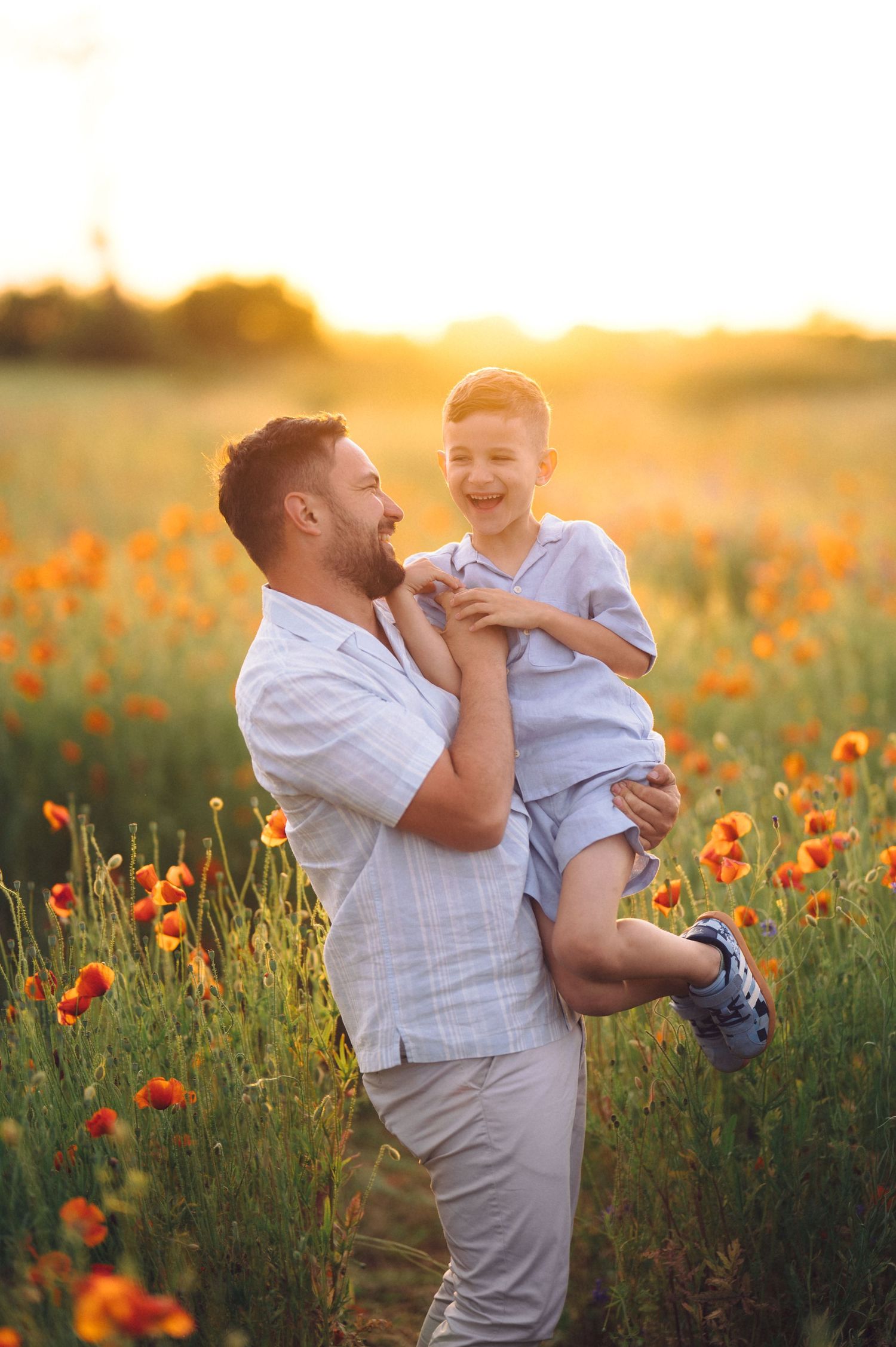 A tender moment at sunset in a poppy field as a parent holds a child while both share joyful laughter.