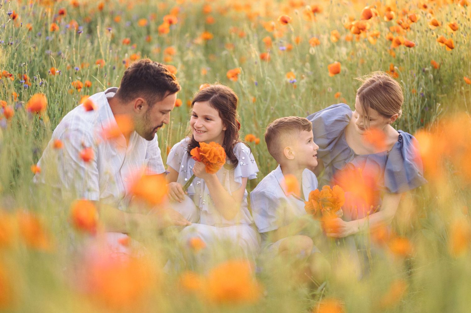 A loving family sits together in a vibrant field of orange poppies during golden hour.