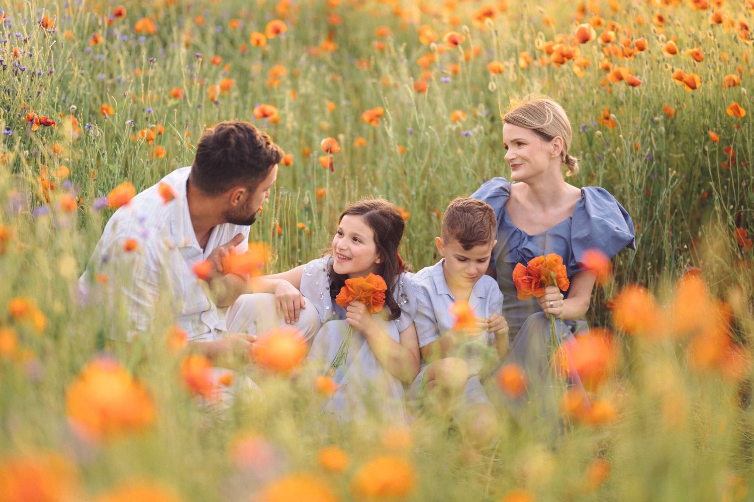 Family sits together in vibrant orange poppies field on a sunny summer day.