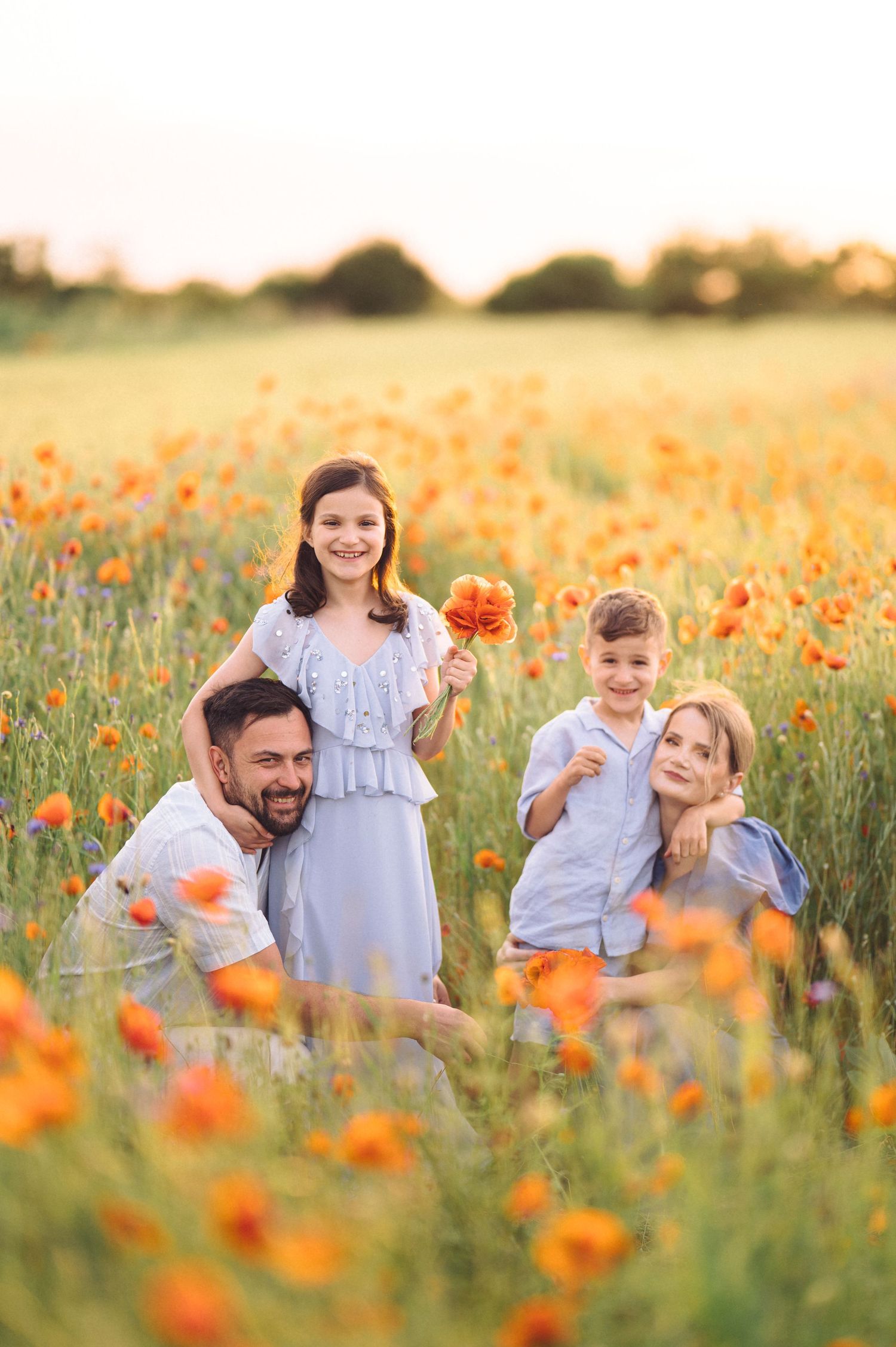 A family enjoys a sunset moment together in a vibrant orange poppy field during golden hour.