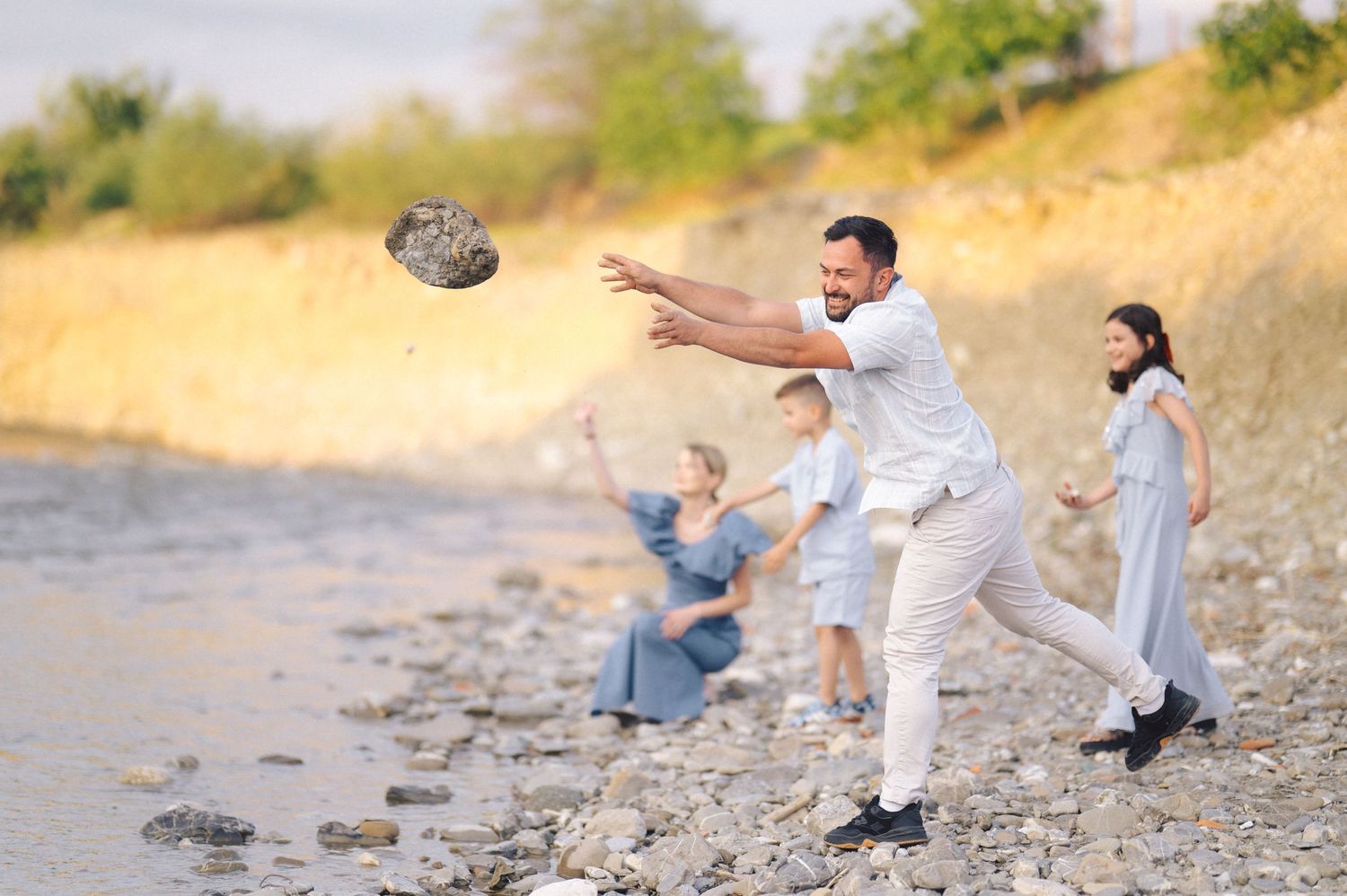 People playing and throwing stones by the riverside on a sunny afternoon in casual white outfits.