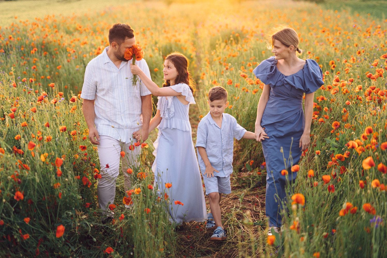 A family walks hand in hand through a stunning meadow filled with bright orange wildflowers.