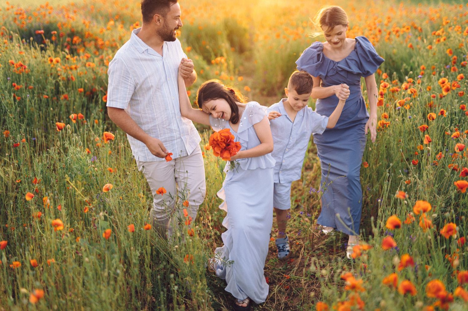 Family enjoying a summer evening together in a field of vibrant orange poppies at golden hour.