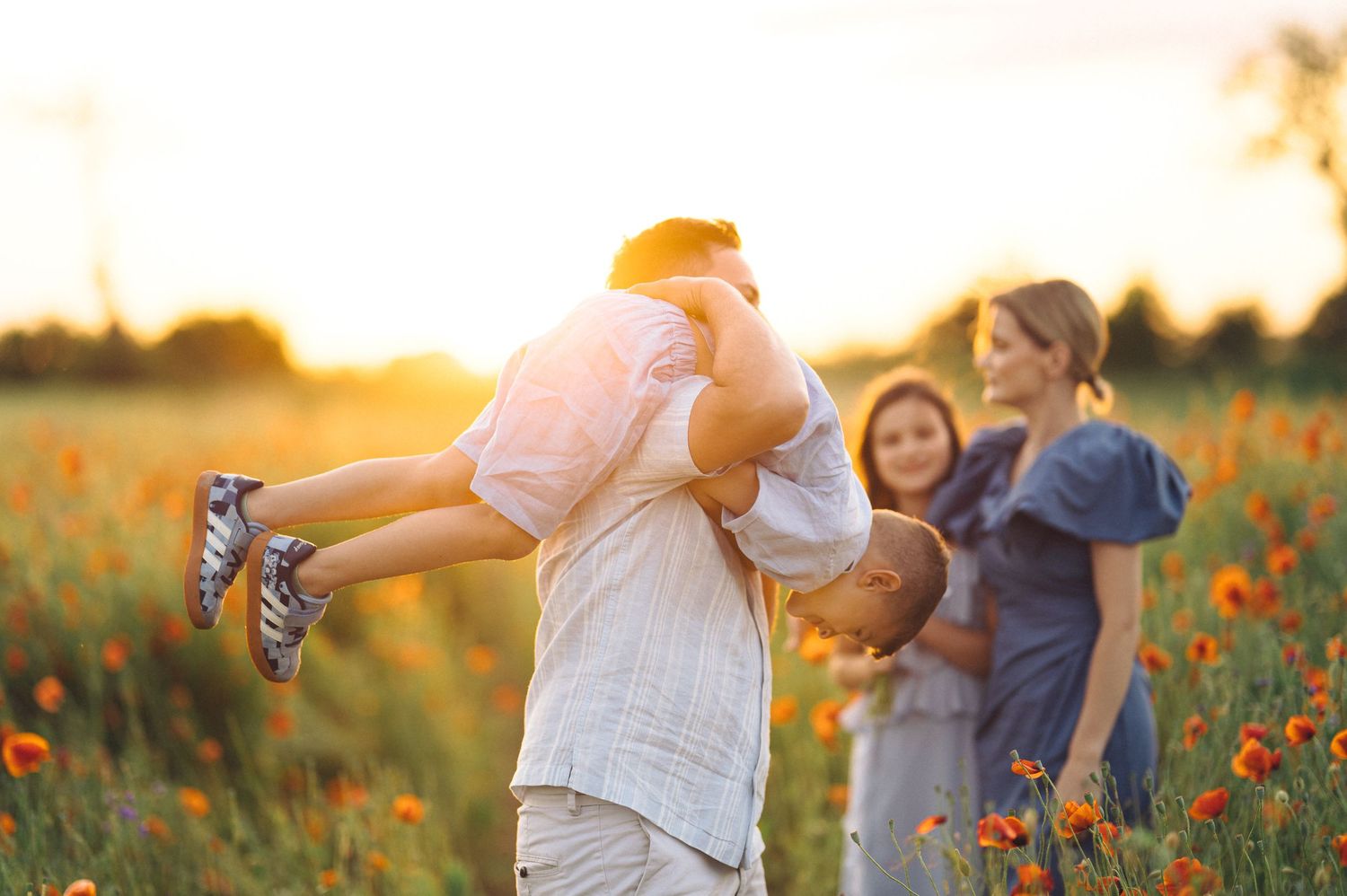 Blurred couple dancing together in a golden sunset poppy field as light glows through wildflowers.