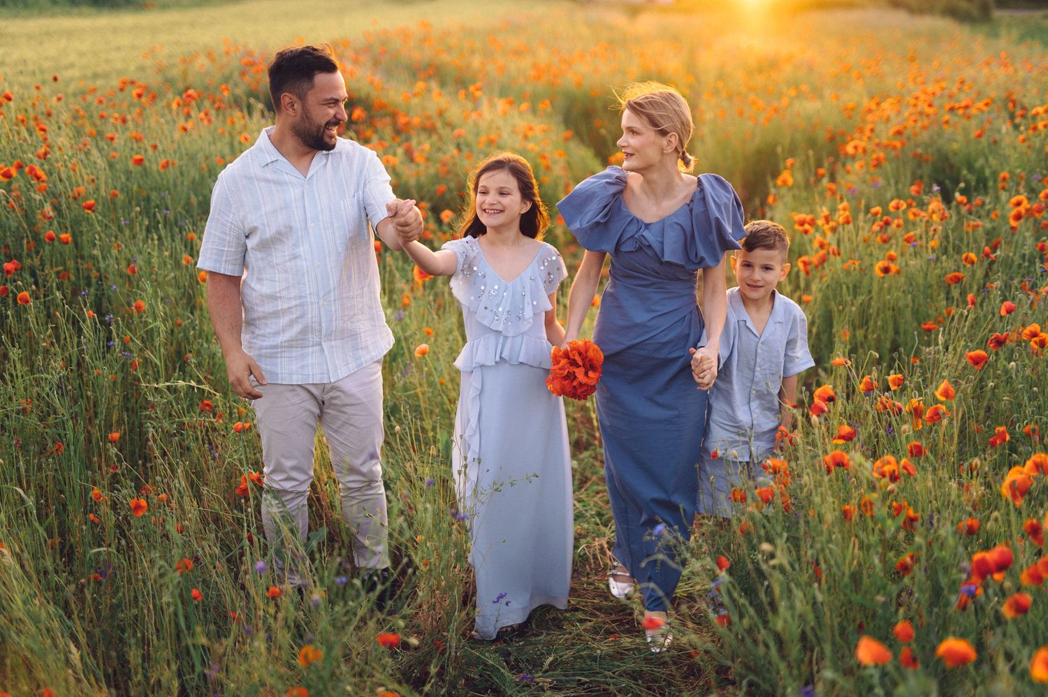 Family walking together through a vibrant orange poppy field at sunset in summer meadow.