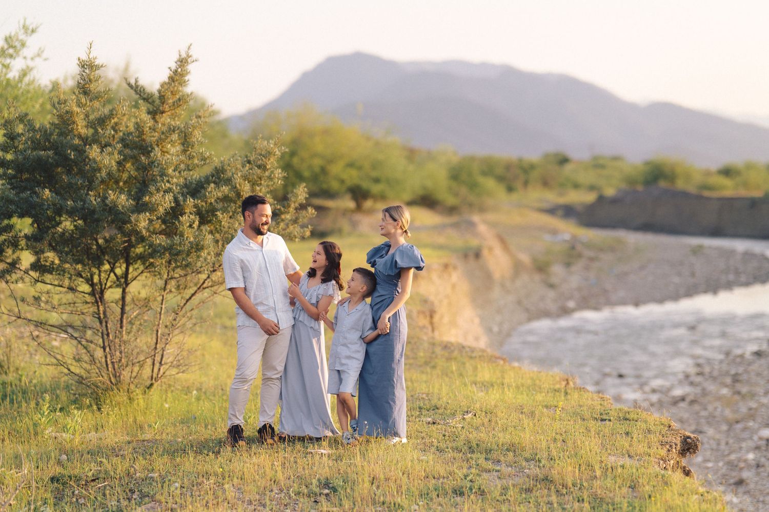A group enjoying a peaceful moment together on a grassy hill overlooking a scenic river landscape at sunset.