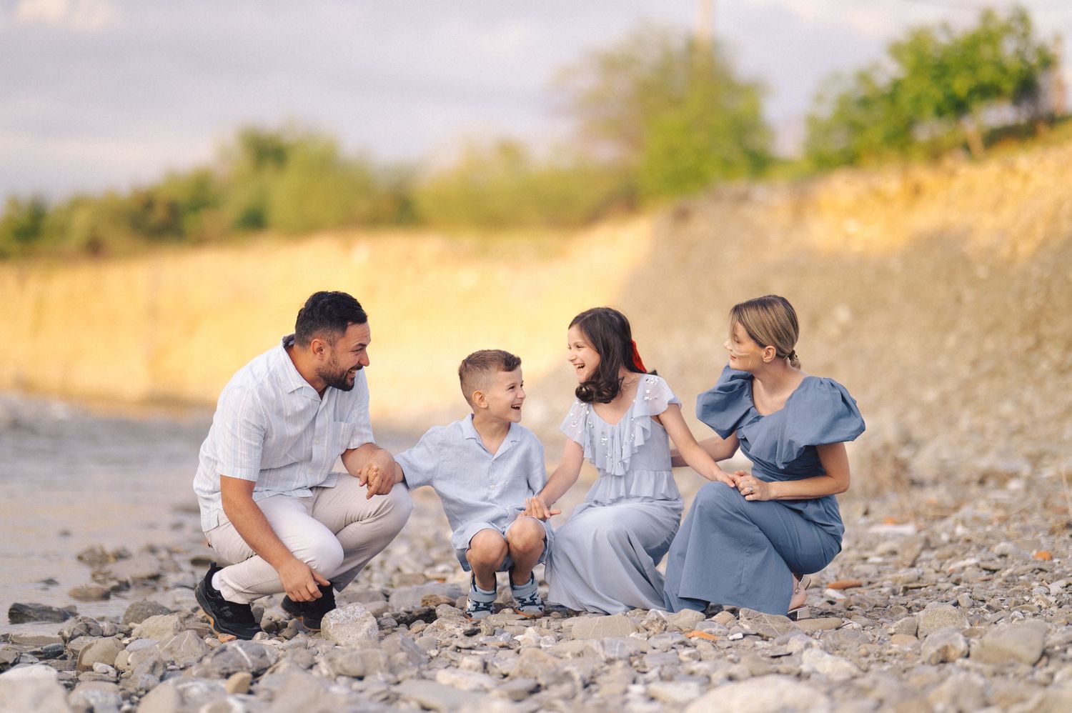 A family sits together on a rocky beach enjoying candid moments in coordinated neutral outfits at sunset.