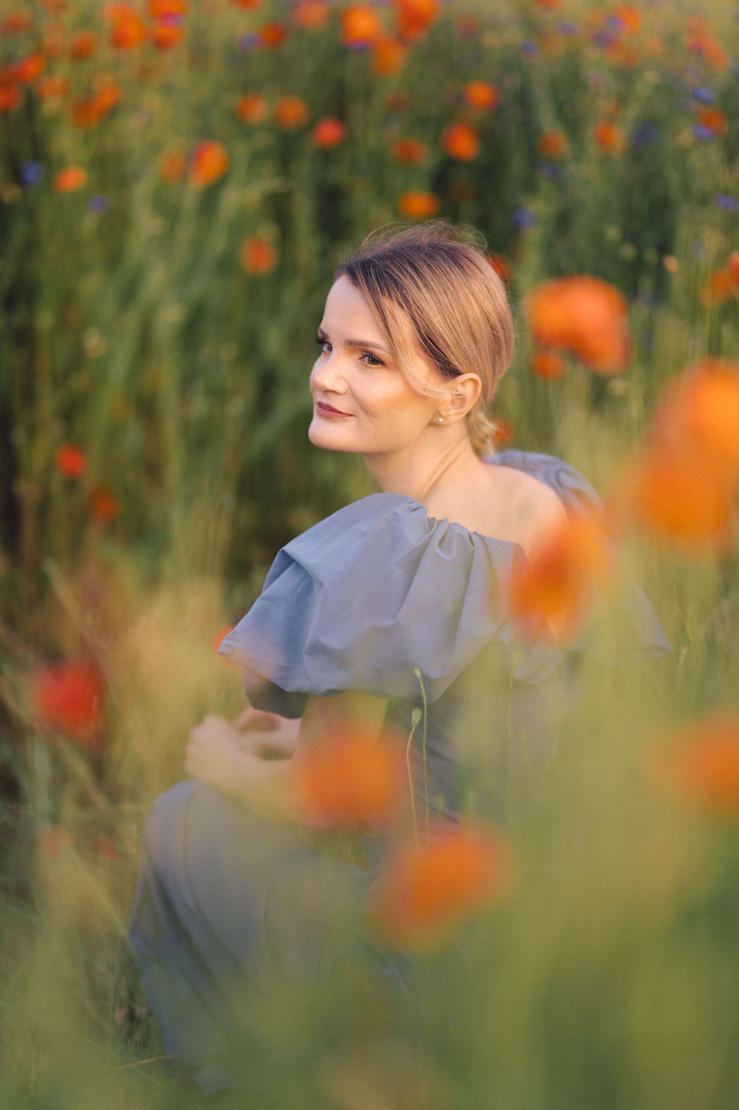 Portrait in a field of orange poppies with soft dreamy bokeh and a light blue ruffled dress.