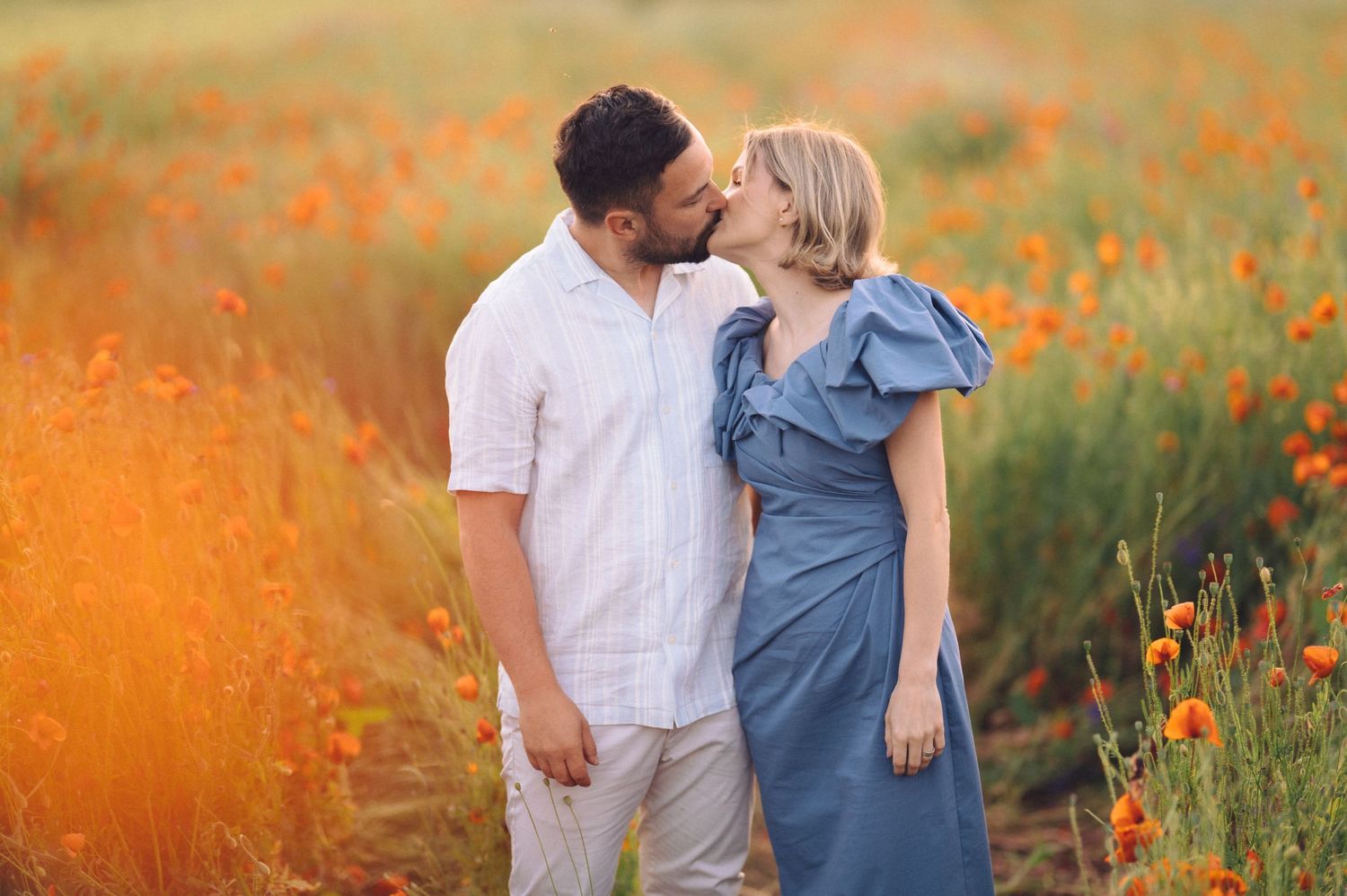 Couple strolls through vibrant orange wildflower meadow at golden hour in warm summer light.