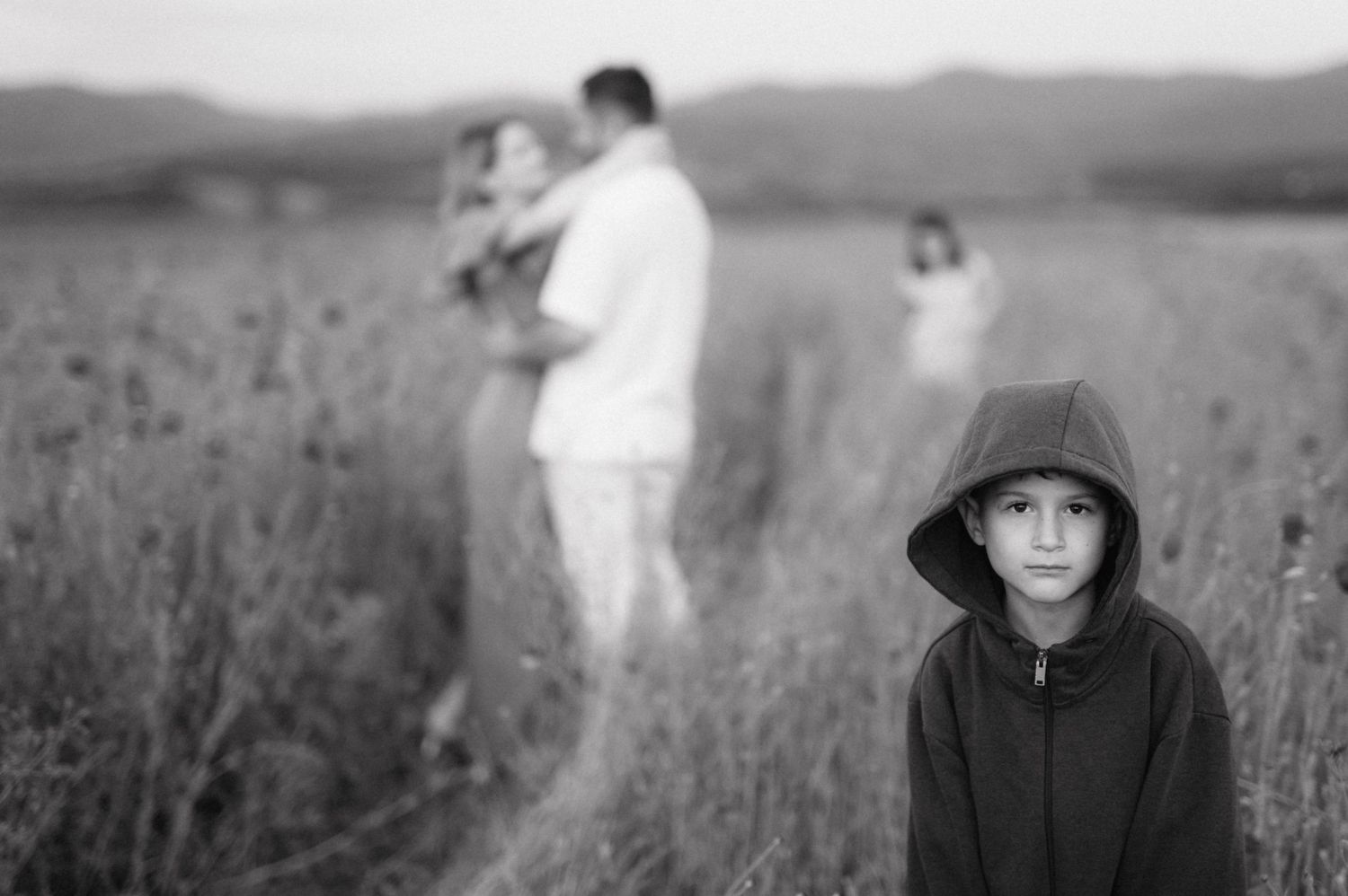 A monochrome portrait of figures in a misty field with a person in the foreground wearing a hooded jacket.