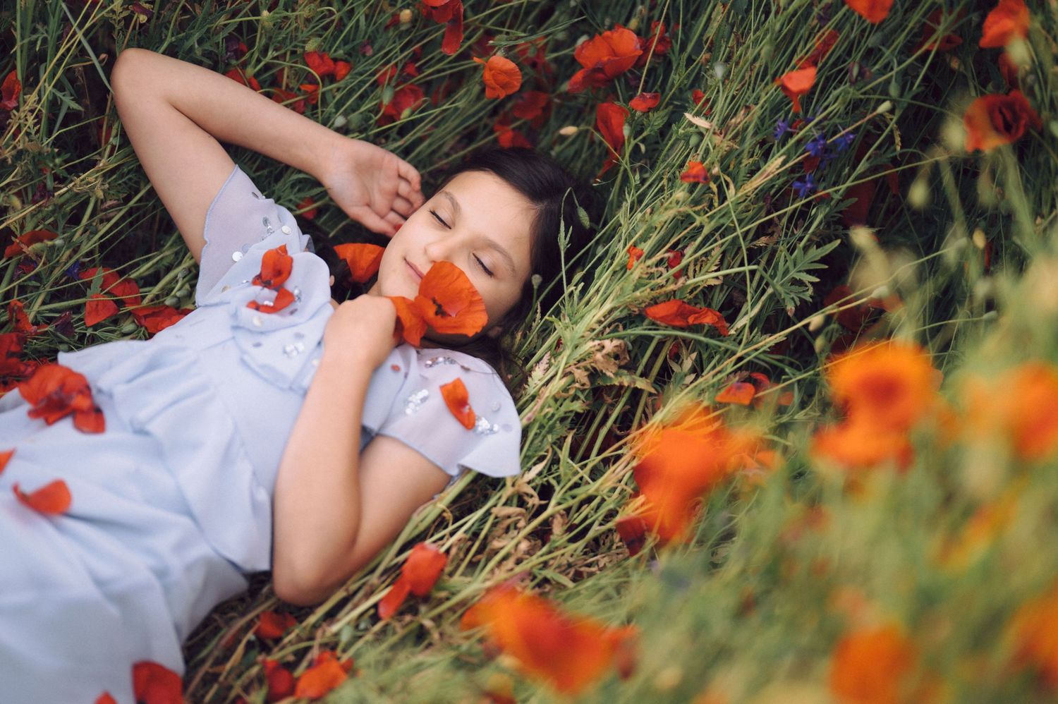 Person in white dress lying peacefully among vibrant orange and red wildflowers in a lush green meadow.