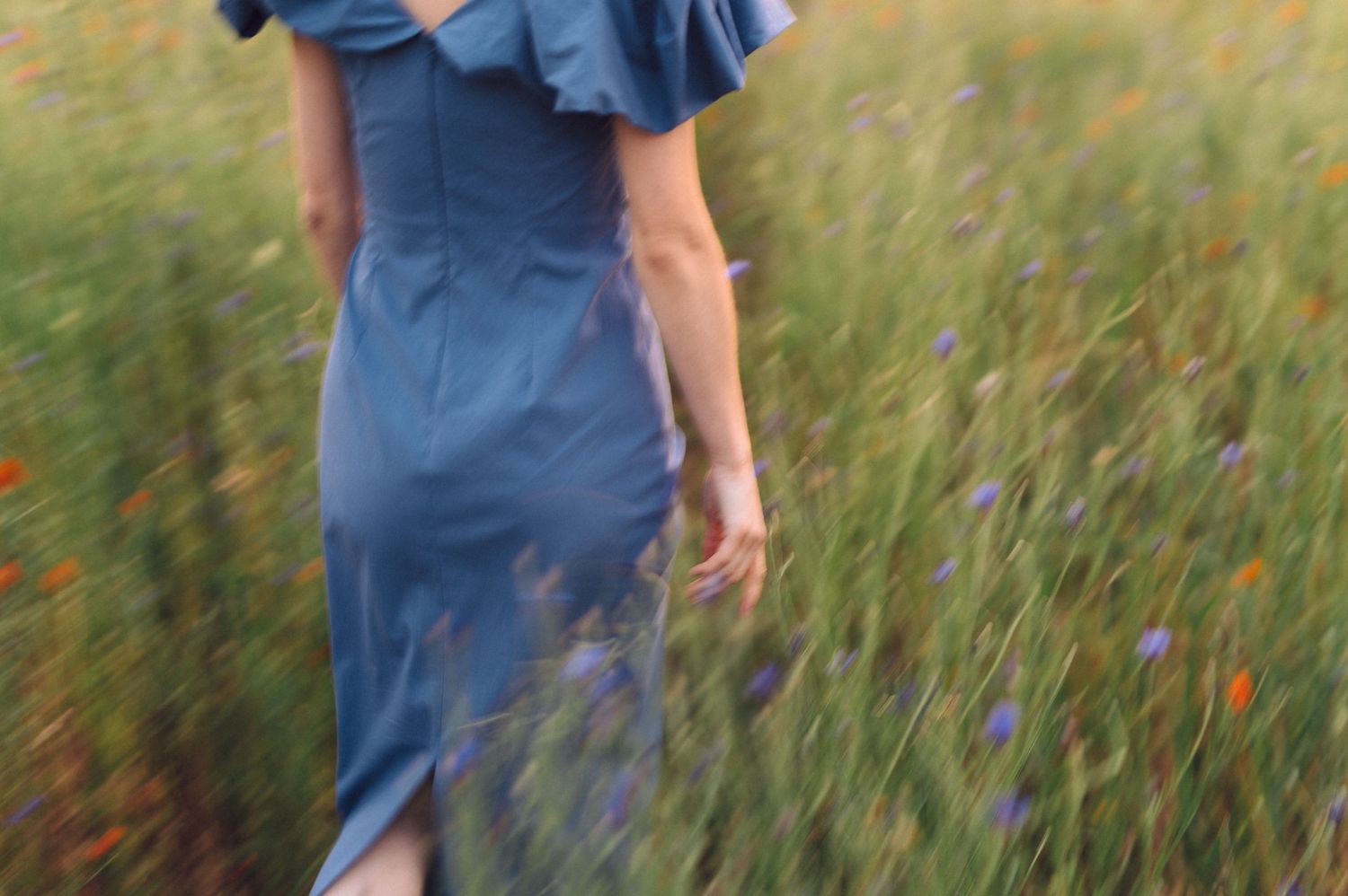 A person wearing blue denim overalls walks through a tall grassy field with lush green vegetation.