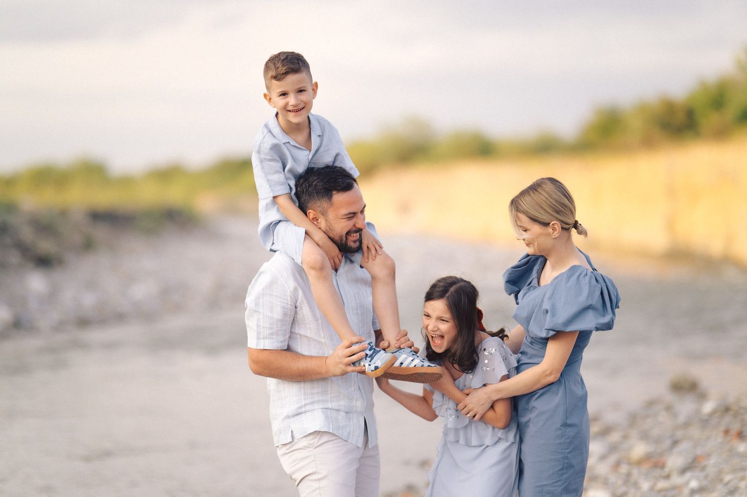 Family plays and laughs together on a sunny beach with soft golden light during sunset.
