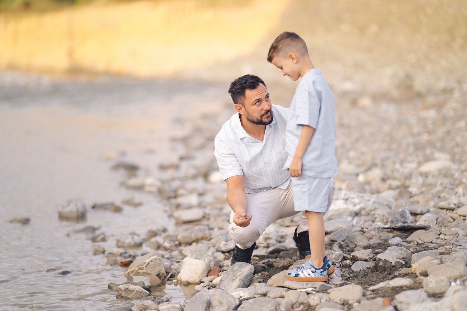 Two people explore and dig along a rocky beach shoreline in casual summer attire on an overcast day.