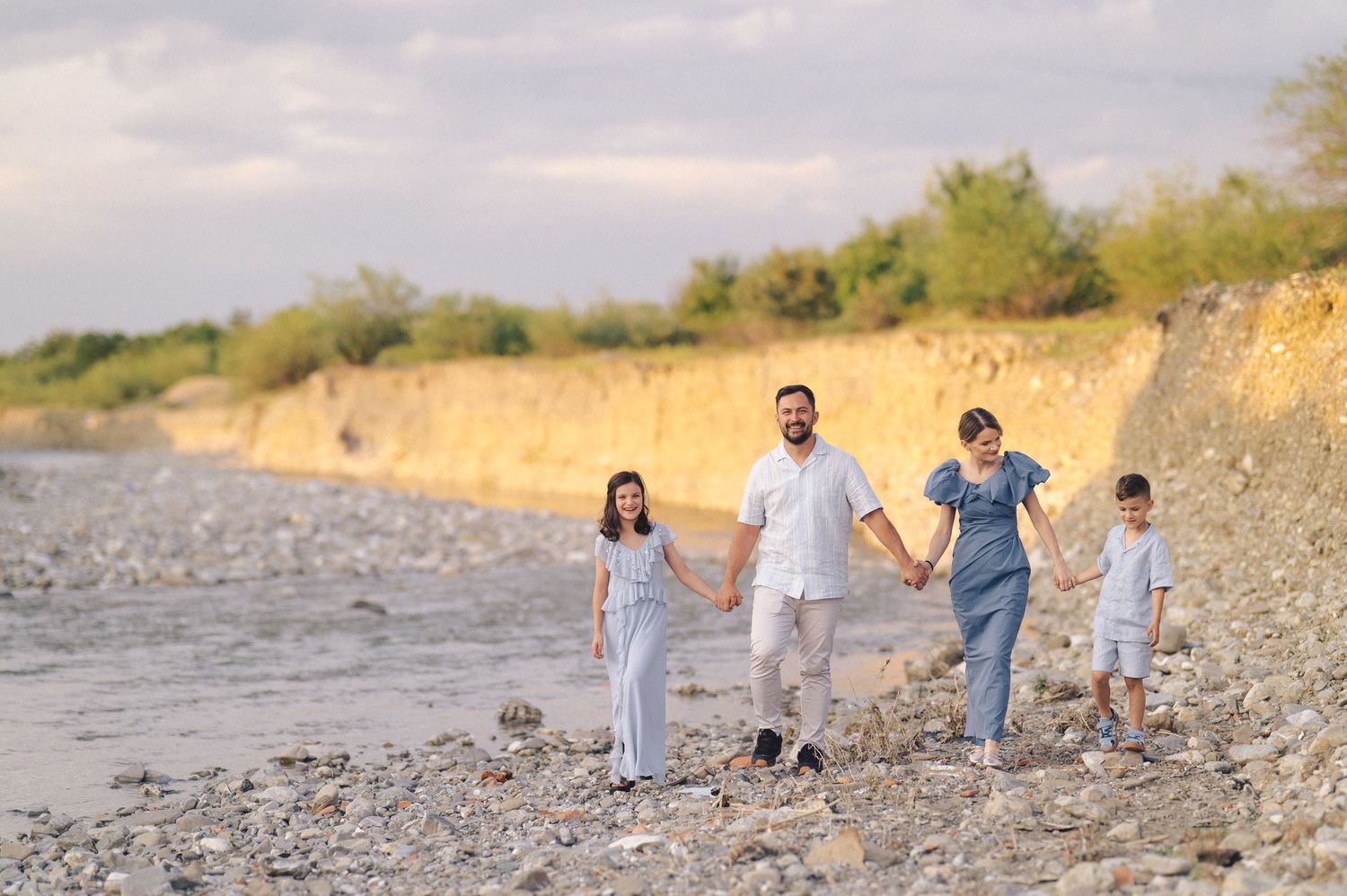 A group walks along a scenic rocky beach shoreline at sunset with mountains in the background.