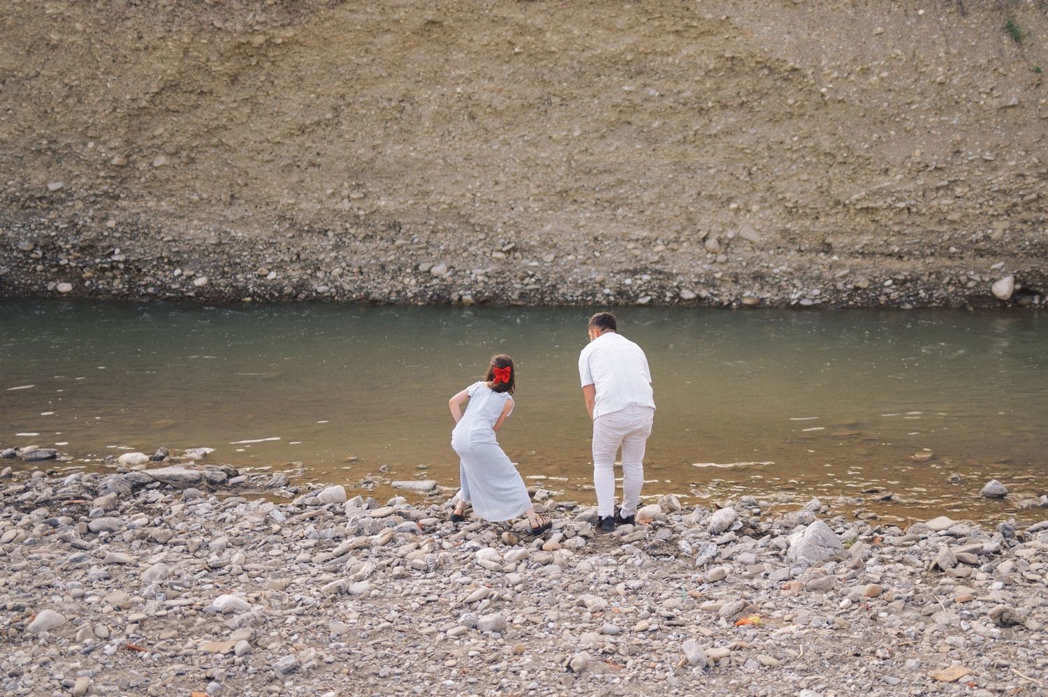 People in protective gear carefully working along a muddy riverbank to assess environmental conditions and take samples.