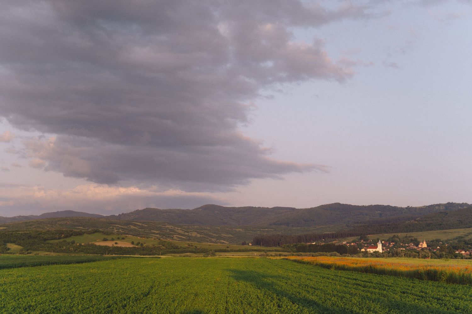 Panoramic mountain landscape with dramatic stormy clouds at sunset over rolling hills and distant peaks.