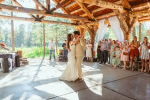 Couple sharing their first dance in a sunlit wooden pavilion surrounded by guests.