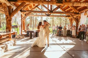 A couple dancing together in a rustic wooden pavilion with sunlight streaming through the beams.