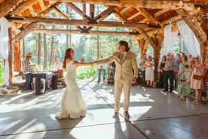 Couple performs their first dance in a rustic wooden pavilion with natural lighting.