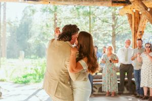 Couple embraces during romantic first dance in rustic timber pavilion with forest backdrop.