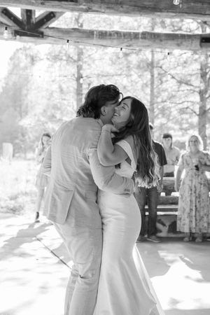 A romantic first dance at a rustic outdoor wedding venue captured in black and white photography.