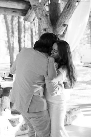A romantic black and white photograph of a couple embracing in a rustic wooden setting with natural light.