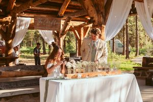 Happy couple cutting their wedding cake at a rustic outdoor venue with wooden beams and white linens.