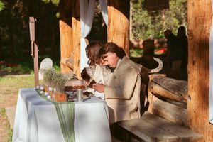 A rustic wooden dining setup decorated with white linens and place settings in a forest setting.
