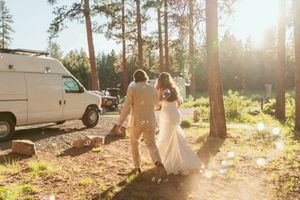Wooded outdoor wedding ceremony setup with white chairs and floral arrangements in a rustic forest setting at sunset.