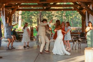 Wedding guests dancing and celebrating under a rustic wooden pavilion with string lights.