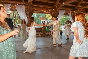 Guests dancing together under a wooden pavilion decorated with string lights at an outdoor reception.