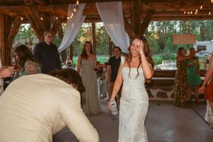 People dancing at a rustic outdoor wedding reception under a covered pavilion with twinkling lights overhead.