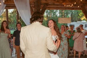 A joyful moment at a rustic outdoor wedding reception under a wooden pavilion with white draping decor and string lights.