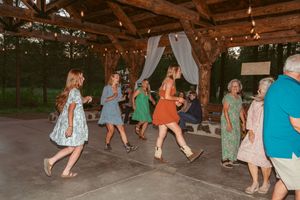 Wedding guests dancing and celebrating in colorful dresses at a rustic outdoor venue with draped fabric decor.