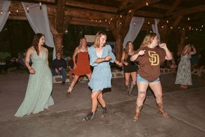 People dancing and celebrating at a rustic barn reception with string lights overhead and white draping decorations.