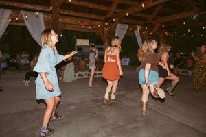 People dancing and having fun at a reception under a wooden pavilion with string lights.