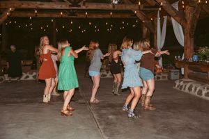 Party guests dance together on a concrete dance floor under string lights at an outdoor reception venue.