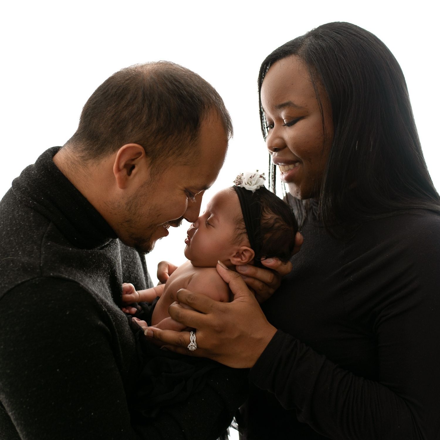 New Mother and father facing each other, holding their newborn baby girl. Father and baby daughter are touching nose.