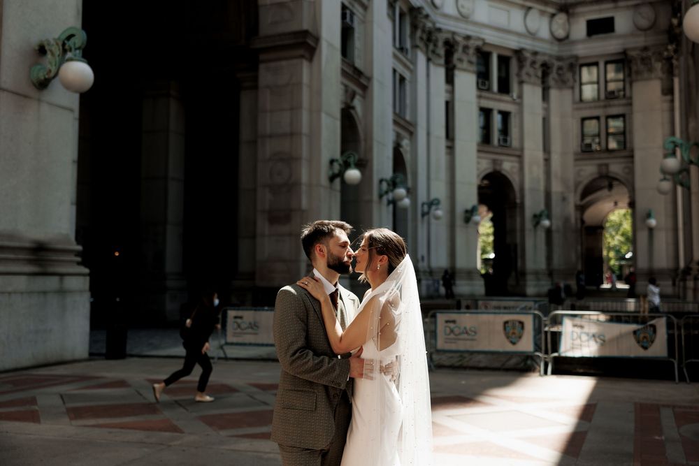 Bride and groom share a tender embrace bathed in golden light outside a grand stone building.
